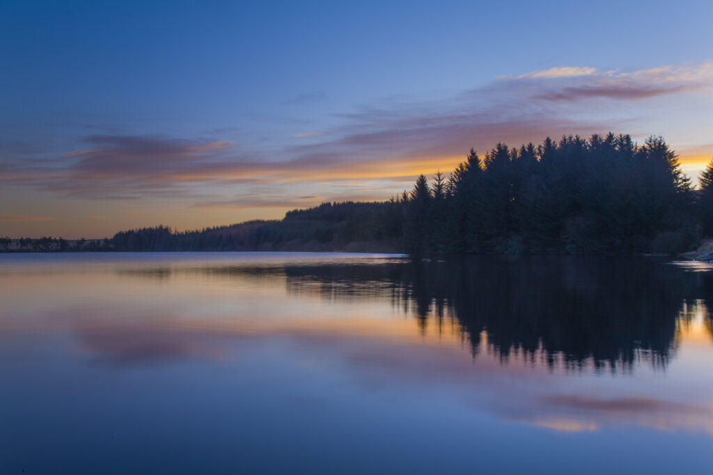 Scotland, Scottish Borders, Alemore Loch. Sunrise reflected in the tranquil waters of the Alemoor Loch, a popular place for recreational fishing near the town of Hawick.
