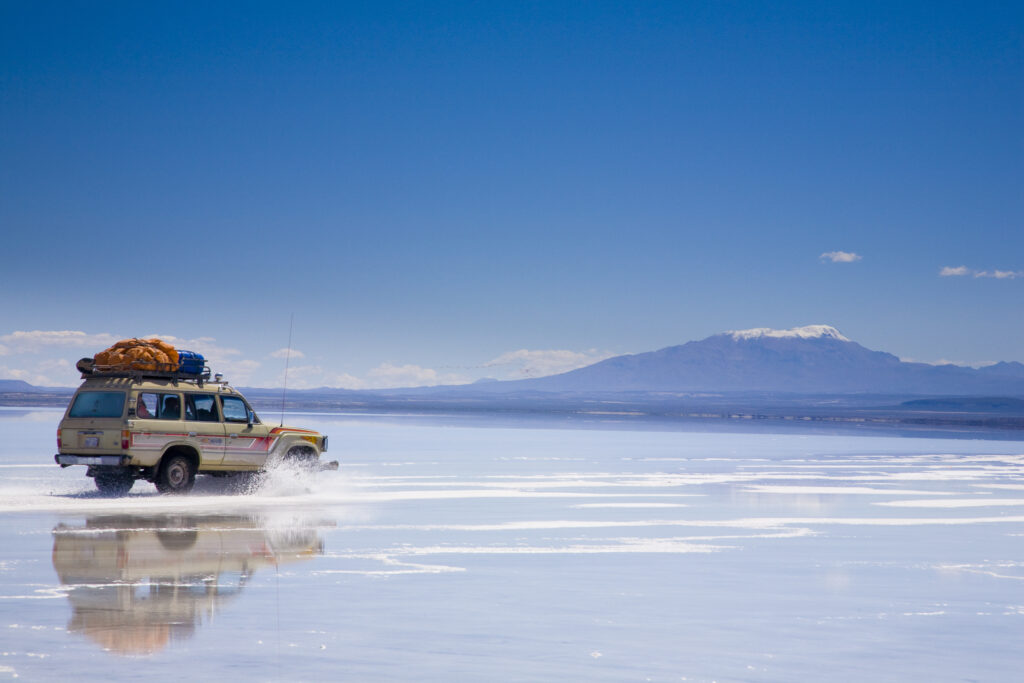 Bolivia, Southern Altiplano, Salar de Uyuni. Tourist jeep crossing the Salar de Uyuni salt flat.