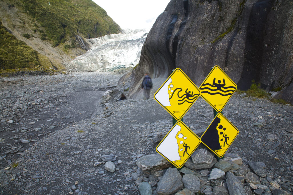 NEW ZEALAND, Westland, Westland National Park. Tourists pass numeous safety signs to explore the mouth of the Franz Josef Glacier.