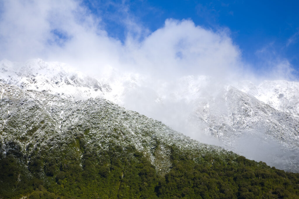 NEW ZEALAND, Westland, Westland National Park. Clouds clear to reveal a fresh snow fall on the Southern Alps near the Fox Glacier.