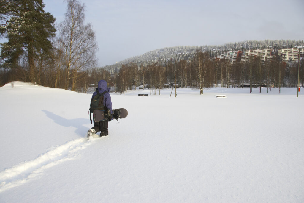 Norway, Oslo, Oslo City. A female snow boarder hikes through a snowfall near Bogstad and the Tryvann Ski field.