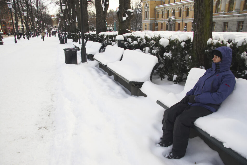 Norway, Oslo, Oslo City. Tourist sitting on a snow covered bench on Karl Johans street in the city of Oslo.