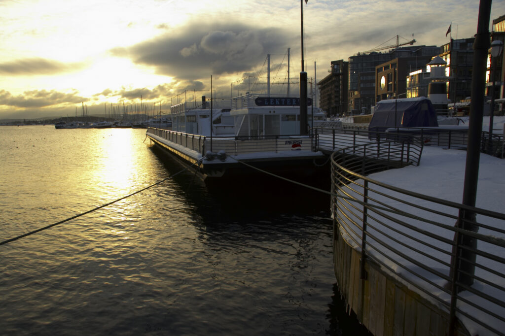 Norway, Oslo, Oslo City. Sunset over the waters of the Oslofjorden Fjord, and surrounding snow covered Aker Quay.