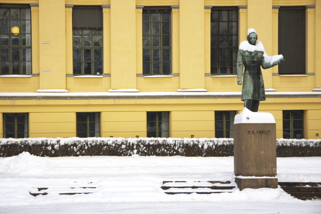 Norway, Oslo, Oslo City. Statue in front of the impressive architecture of the University Of Oslo Buildings, surrounded by snow.