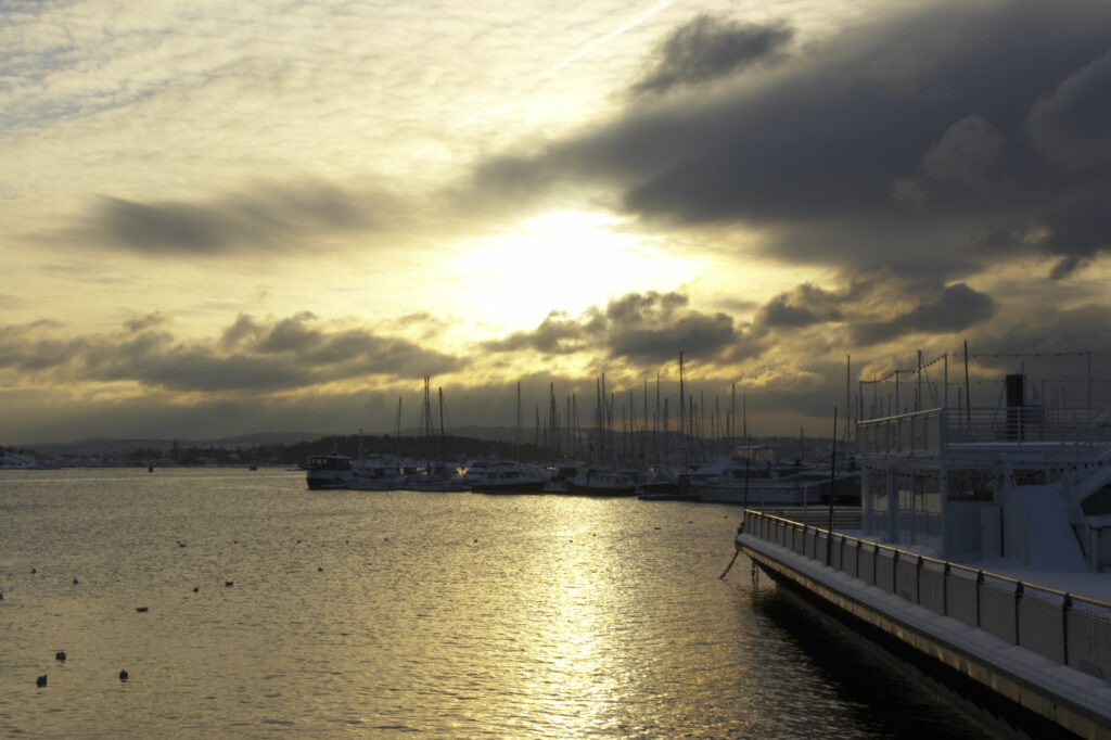Norway, Oslo, Oslo City. Sunset over the waters of the Oslofjorden Fjord, and surrounding snow covered Aker Quay.