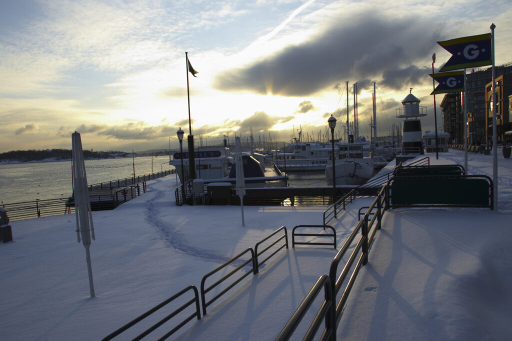 Norway, Oslo, Oslo City. Late afternoon winter light illuminates the snow coverered Aker Quay and the Oslofjorden Fjord.