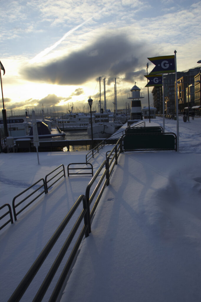 Norway, Oslo, Oslo City. Late afternoon winter light illuminates the snow coverered Aker Quay and the Oslofjorden Fjord.