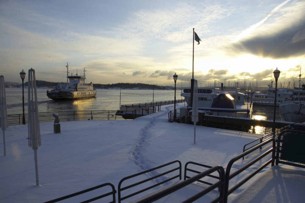 Norway, Oslo, Oslo City. Late afternoon winter light illuminates the snow coverered Aker Quay and the Oslofjorden Fjord.