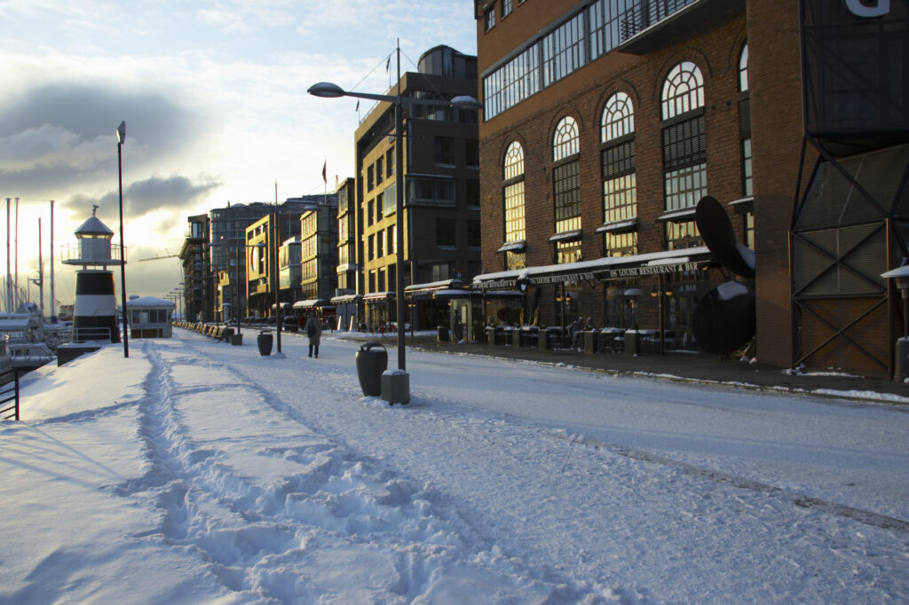 Norway, Oslo, Oslo City. Late afternoon winter light illuminates the snow coverered Aker Quay and the Oslofjorden Fjord.