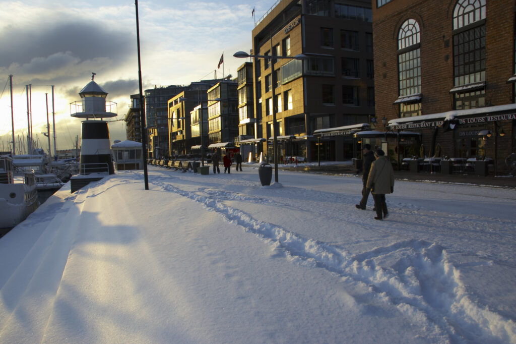 Norway, Oslo, Oslo City. Late afternoon winter light illuminates the snow coverered Aker Quay and the Oslofjorden Fjord.