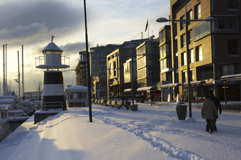 Norway, Oslo, Oslo City. Late afternoon winter light illuminates the snow coverered Aker Quay and the Oslofjorden Fjord.