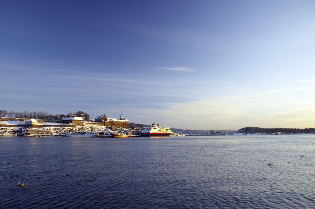 Norway, Oslo, Oslo City. Late afternoon winter light illuminates the snow coverered Aker Quay and the Oslofjorden Fjord.