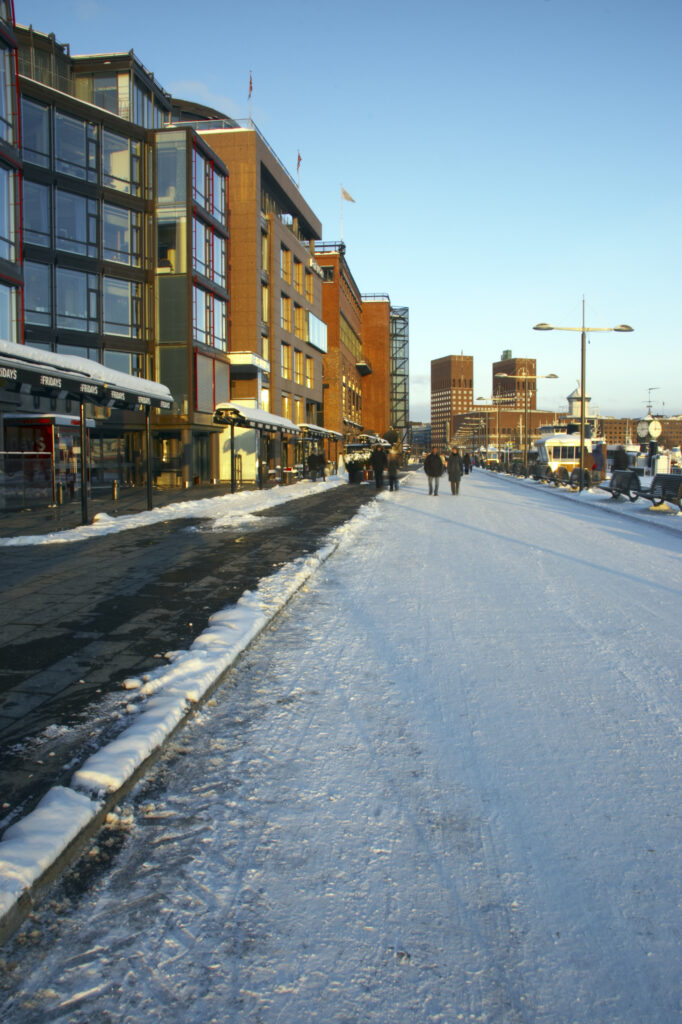 Norway, Oslo, Oslo City. Late afternoon winter light illuminates the snow coverered Aker Quay and the Oslofjorden Fjord.