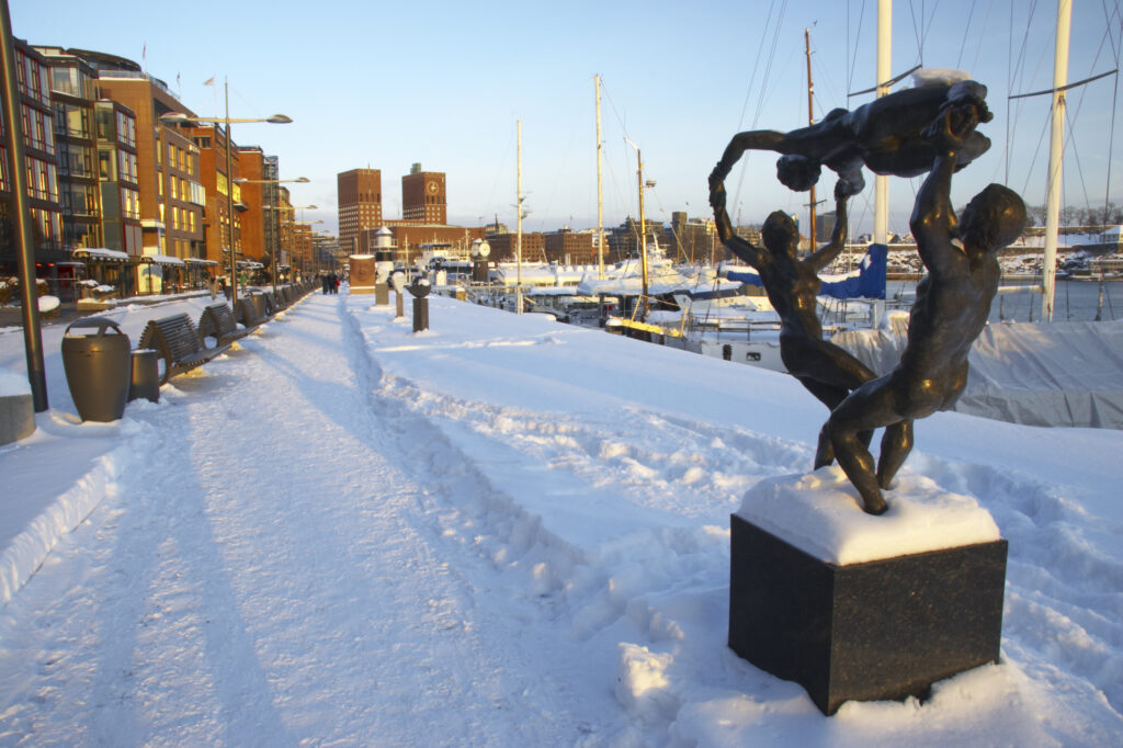 Norway, Oslo, Oslo City. Late afternoon winter light illuminates the snow coverered Aker Quay and the Oslofjorden Fjord.