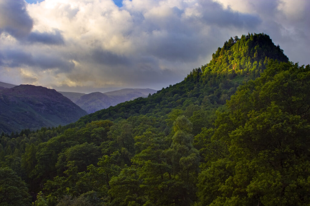 ENGLAND, Cumbria, Lake District National Park. A brief shaft of light illuminates Castle Crag and surrounding hills of Borrowdale