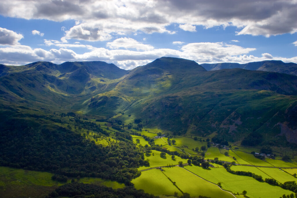ENGLAND, Cumbria, Lake District National Park. A clearing storm allows sunlight to break through onto agricultural land and surrounding fells of Grisedale Valley.
