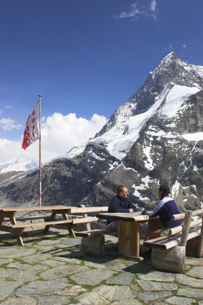 Switzerland, Valais, The Matterhorn. A brother and sister enjoy the fine views of the alps from benches outside Schonbielhutte