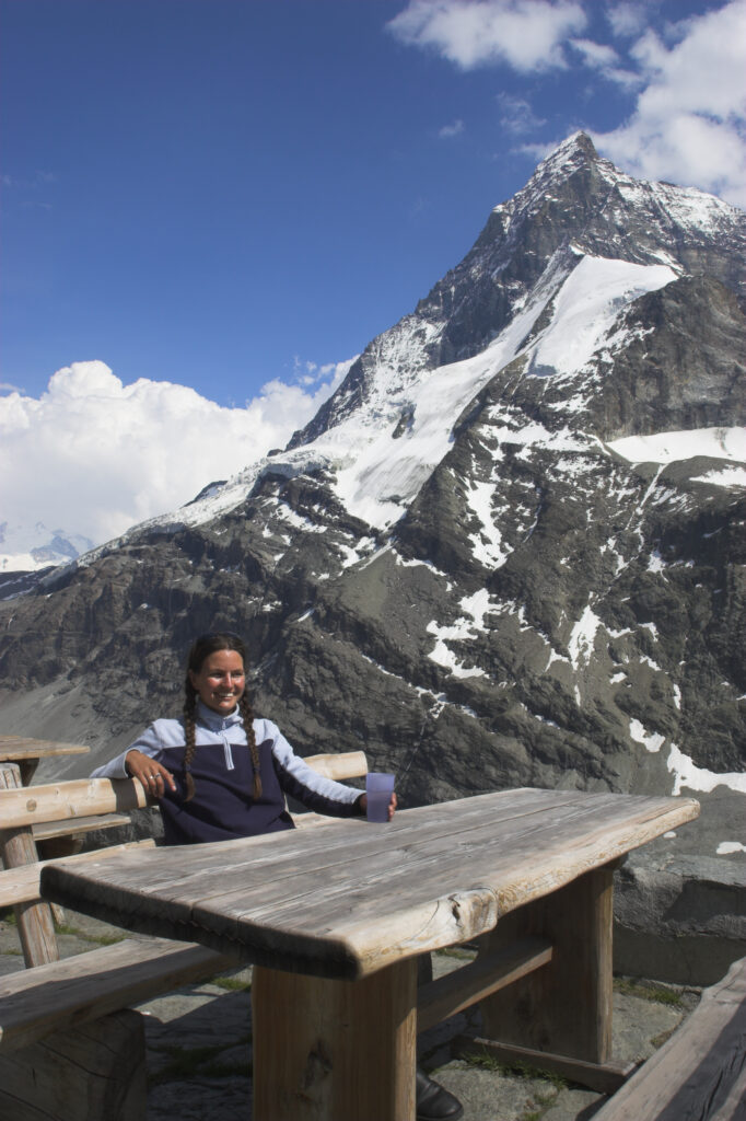 Switzerland, Valais, The Matterhorn. A girl in her mid 20s enjoys a drink and fine views of the alps from outside Schonbielhutte