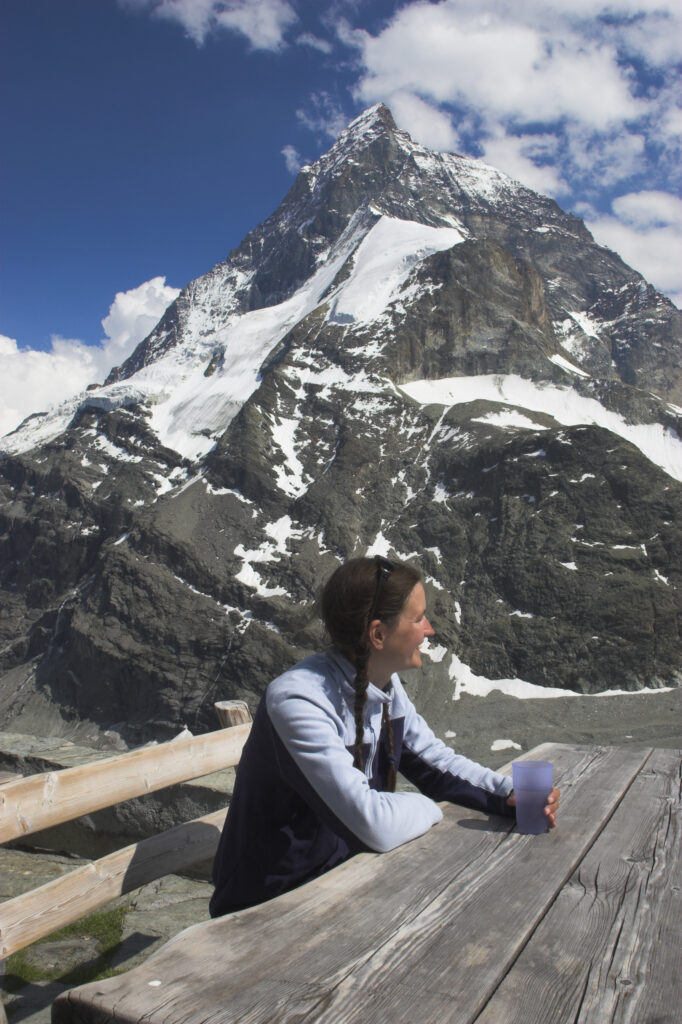 Switzerland, Valais, The Matterhorn. A girl in her mid 20s enjoys a drink and fine views of the alps from outside Schonbielhutte