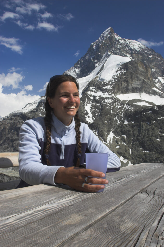 Switzerland, Valais, The Matterhorn. A girl in her mid 20s enjoys a drink and fine views of the alps from outside Schonbielhutte