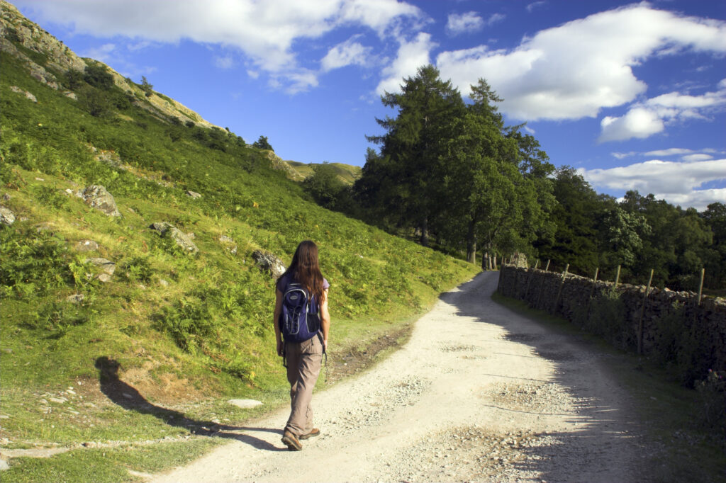England, Cumbria, Lake District National Park. A female hiker walking along a well formed public footpath in Patterdale.