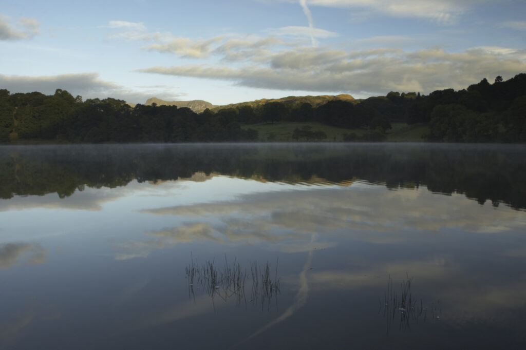 England, Cumbria, Lake District National Park Reflections of typical lake district scenary in the still waters of Loughrigg Tarn