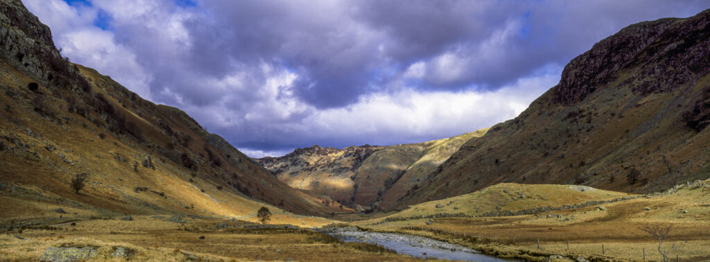 England, Cumbria, Lake District National Park. Brief shafts of sun illuminate the surrounding peaks of the Langstrath Valley.