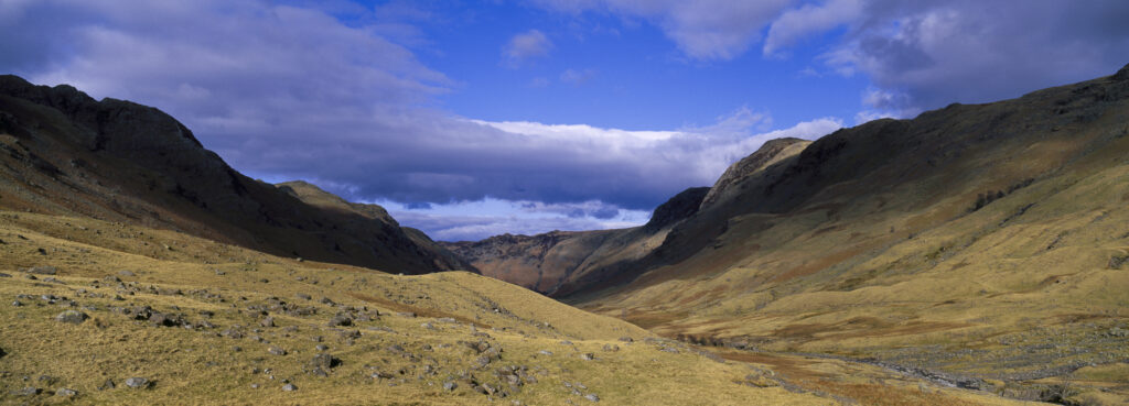 England, Cumbria, Lake District National Park. Brief shafts of sun illuminate the surrounding peaks of the Langstrath Valley.