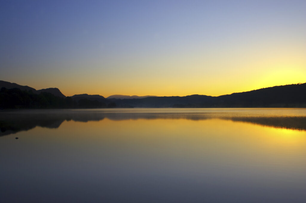 England, Cumbria, Lake District National Park. Dawn looking across the still waters of Coniston Water, within the Lake District National Park.