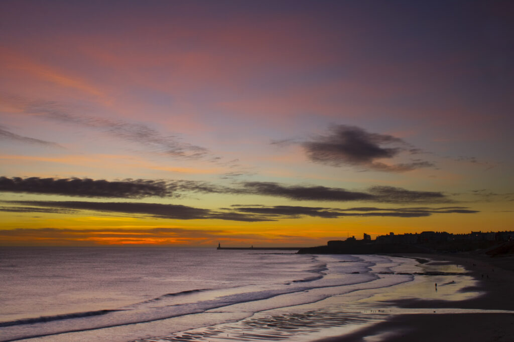 England, Tyne and Wear, Tynemouth. Sunrise looking across longsands towards the North Tyne Pier lighthouse and the Tynemouth priory.