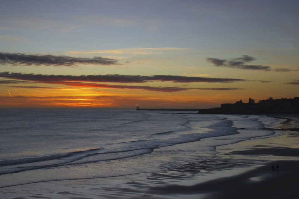 England, Tyne and Wear, Tynemouth. Sunrise looking across longsands towards the North Tyne Pier lighthouse and the Tynemouth priory.
