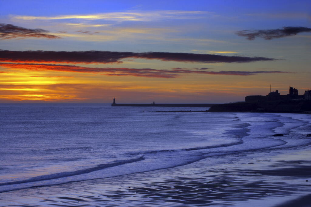 England, Tyne and Wear, Tynemouth. Sunrise looking across longsands towards the North Tyne Pier lighthouse and the Tynemouth priory.