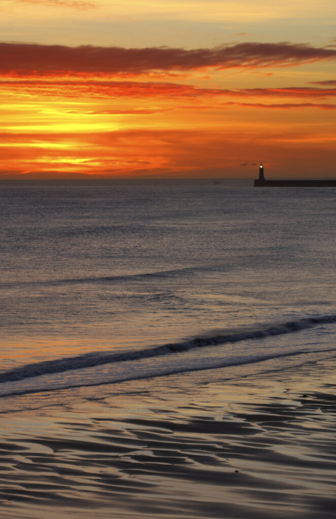 England, Tyne and Wear, Tynemouth. Sunrise looking across longsands towards the North Tyne Pier lighthouse.