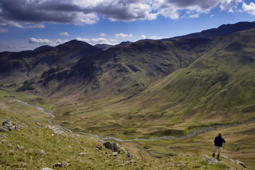 England, Cumbria, Lake District National Park. A hiker admires the impressive wild scenery of the Mickleden Valley.