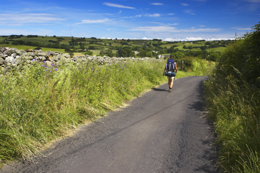England, Cumbria, Lake District National Park. Female hiker walking down a country lane near Caldbeck.
