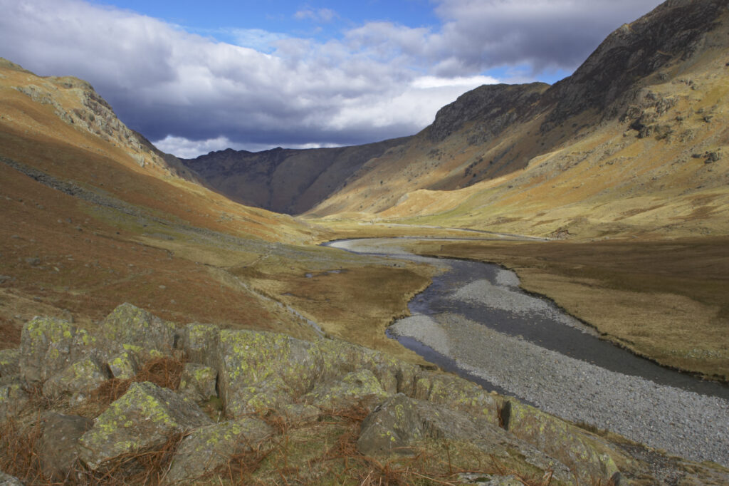 England, Cumbria, Lake District National Park. Brief shafts of sun illuminate the surrounding peaks of the Langstrath Valley.
