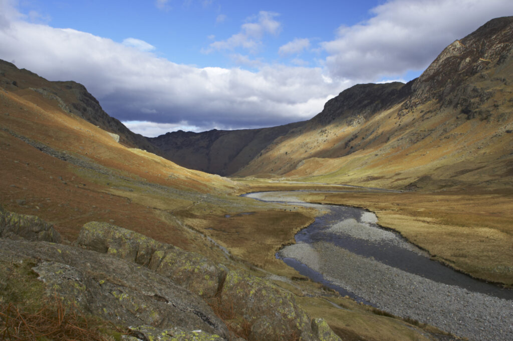 England, Cumbria, Lake District National Park. Brief shafts of sun illuminate the surrounding peaks of the Langstrath Valley.