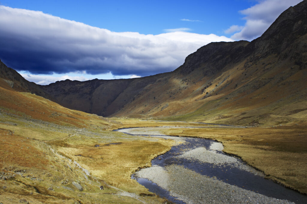 England, Cumbria, Lake District National Park. Brief shafts of sun illuminate the surrounding peaks of the Langstrath Valley.