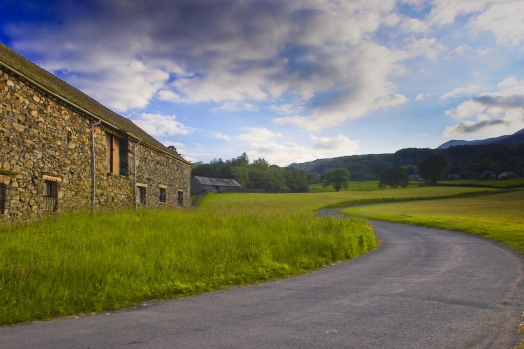 England, Cumbria, Lake District National Park. Soft evening light illuminates a small country lane and a stone farm building
