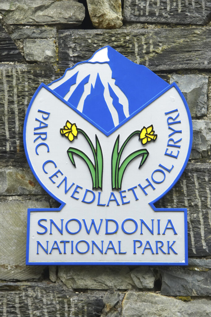 Wales, Caernarfonshire, Snowdonia National Park. Snowdonia National Park sign on traditional stone wall, located in the town of Betws-y-Coed.