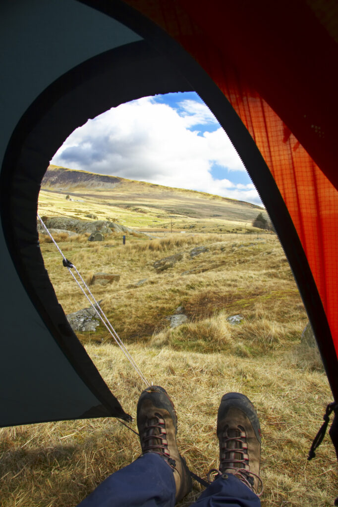 Wales, Caernarfonshire, Snowdonia National Park. Hiker admiring the landscape of the Ogwen Valley, from the comfort of his tent.