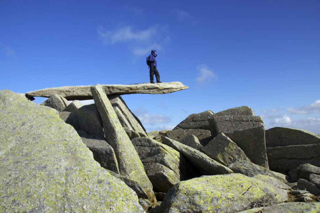 Wales, Caernarfonshire, Snowdonia National Park. Female hiker admiring the landscape from the Cantilever stone, near the peak of the Glyder Fach mountain.