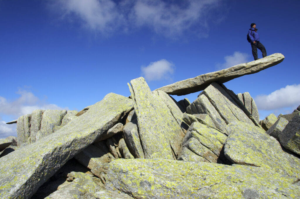 Wales, Caernarfonshire, Snowdonia National Park. Female hiker admiring the landscape from the Cantilever stone, near the peak of the Glyder Fach mountain.