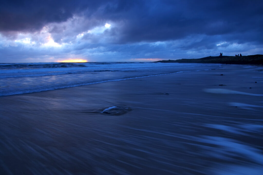 England Northumberland Embleton Bay Dawn over the wild coastline of Embleton Bay overlooked by Dunstanburgh Castle