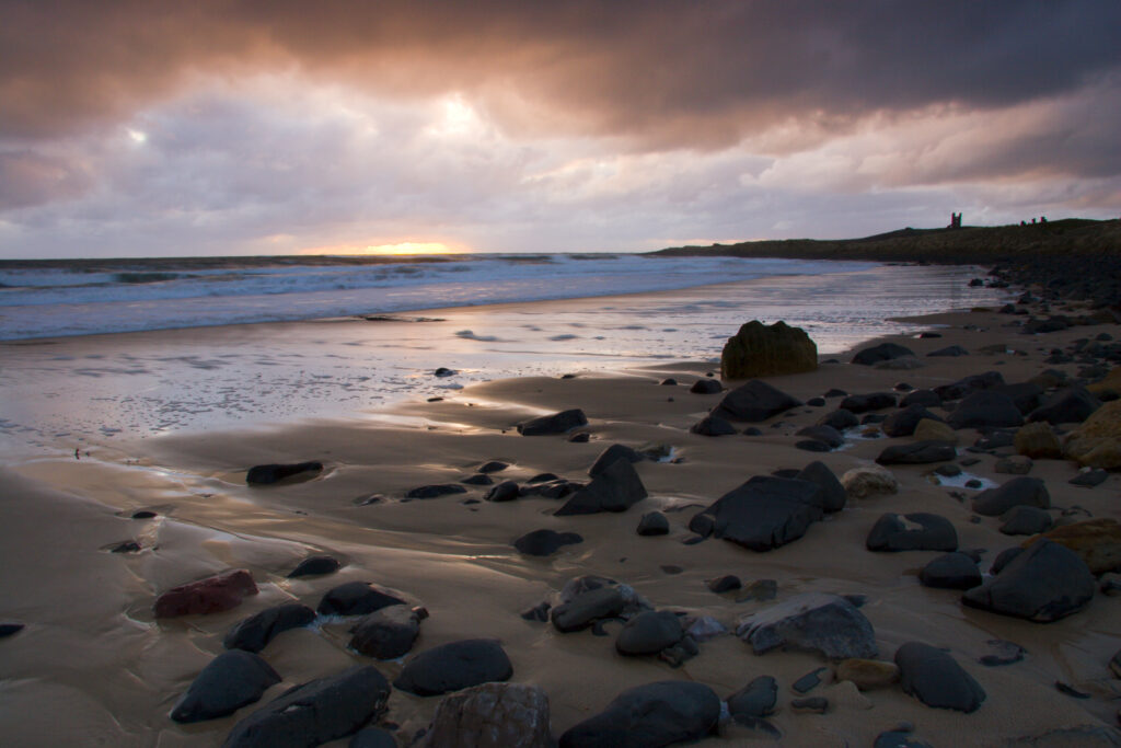 England Northumberland Embleton Bay Dawn over the wild coastline of Embleton Bay overlooked by Dunstanburgh Castle