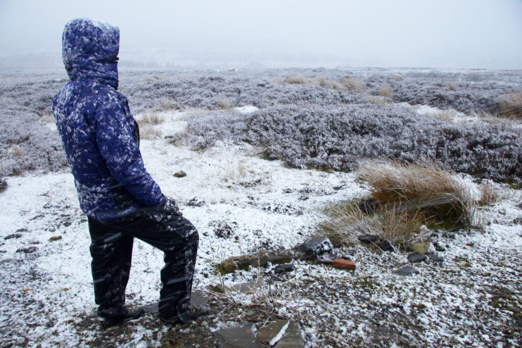 England, North Yorkshire, North York Moors National Park. Female hiker admiring the barren landscape of the moors during a spring snowfall near Eller Beck Bridge.