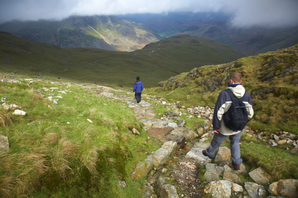 England, Cumbria, Lake District National Park. Hikers descending from tarn towards Dungeon Ghyll in the Great Langdale Valley