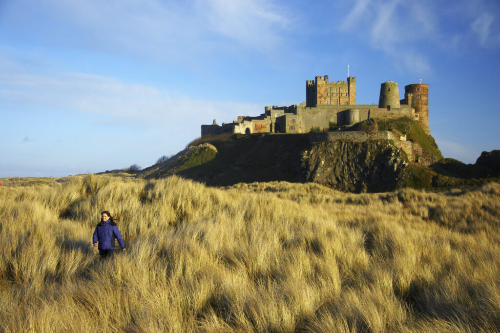 England, Northumberland, Bamburgh Castle. Hiker walking through dunes near Bamburgh castle in Bamburgh.