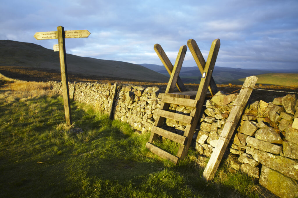 England Northumberland The Pennine Way Ladder Stile over a wall marking the England Scotland border with the Schil in the distance.