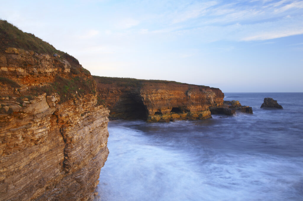 England, Tyne and Wear, Marsden Bay. Early morning light illuminates the crashing waves of the North Sea, near Lizard Point and Marsden Bay.